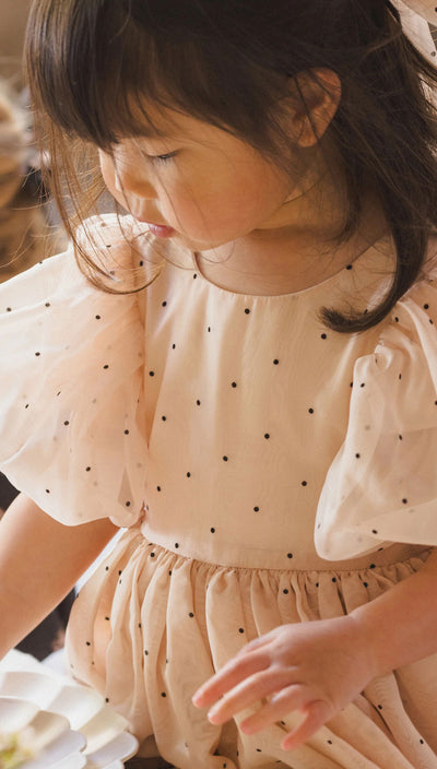 Young girl wearing a beige dress with black polka dots, looking down. SOFIA DRESS | Antique | Noralee