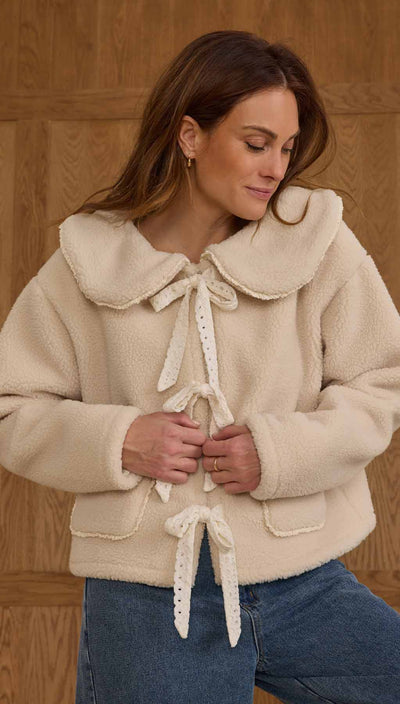 Woman wearing a cream-colored jacket with a large collar against a wooden background. Rylee + Cru Shearling Collared Coat – Natural 