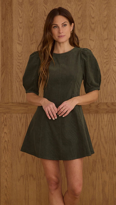 Woman wearing a green dress against a wooden paneled wall. Levi Mini Dress | Evergreen | Rylee + Cru