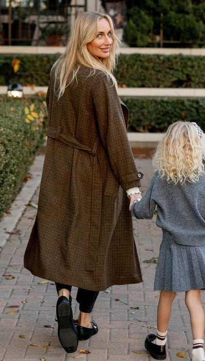 Pretty blonde Woman in a long brown coat by rylee and cru walking with a young girl in a gray coat on a sidewalk.